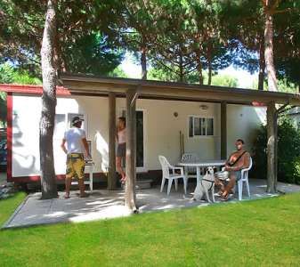 Una veranda con sedie e tavolo all'aperto, persone sedute sotto gli alberi.