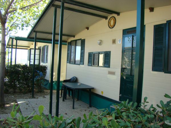 Roulotte con veranda, tavolo e sedie all'esterno, circondata da cespugli.
