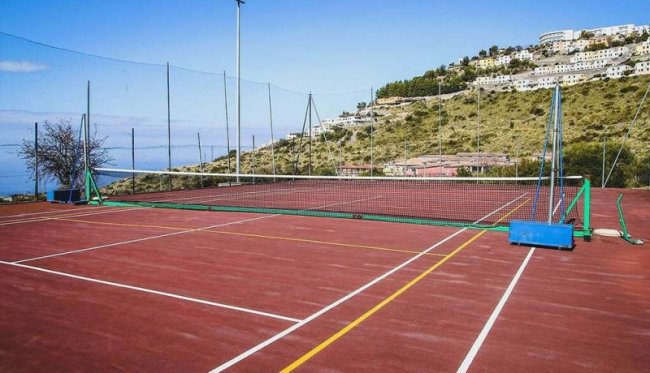 Un campo da tennis rosso con reti, situato su una collina con vista panoramica.