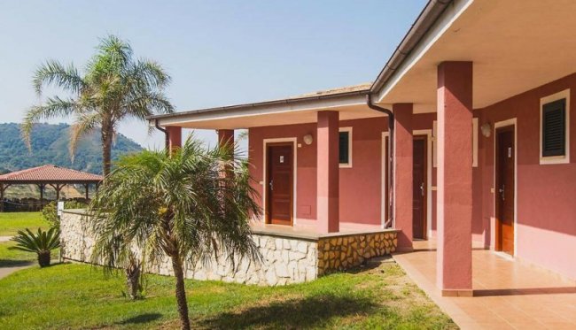 Edificio rosa con colonnato, affiancato da palme e prato verde.