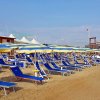 Spiaggia con file di lettini blu e ombrelloni colorati sotto un cielo limpido.