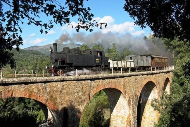 Treno a vapore attraversa un ponte di pietra.