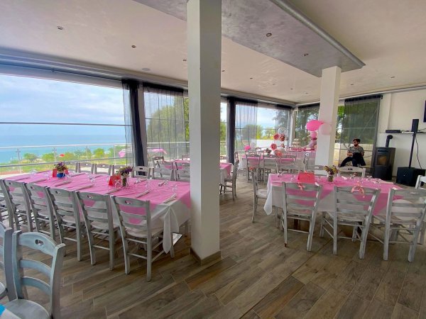 Sala evento con tovaglie rosa e vista sul mare.
