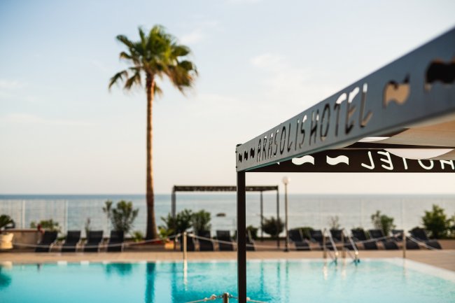 Piscina vista mare con una palma e una tettoia.