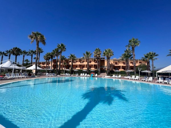 Piscina in un resort, con palme e edificio sullo sfondo sotto un cielo blu.