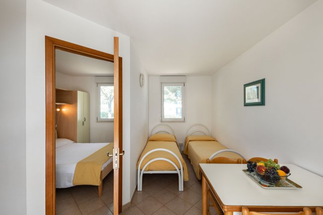 Camera con due letti singoli e una porta aperta su una stanza con letto matrimoniale.