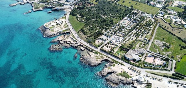 Vista aerea di costa con mare azzurro, verde, edifici e strade.