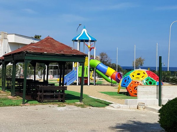 Parco giochi con scivolo, altalene e gazebo in legno.