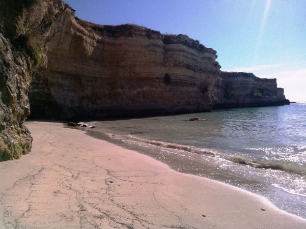 Una spiaggia sabbiosa con onde leggere e alte scogliere rocciose al sole.