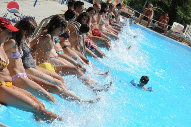 Persone sedute sul bordo di una piscina, schizzando acqua con i piedi.