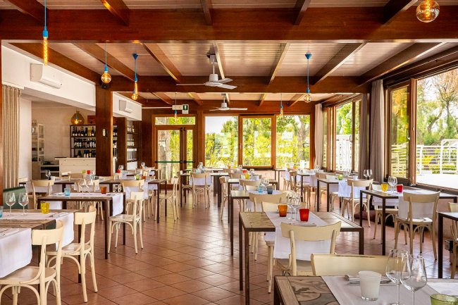 Interno di un ristorante con tavoli apparecchiati e grandi finestre.