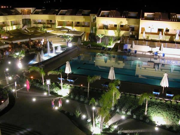 Vista notturna di una piscina con ombrelloni e giardino illuminato.