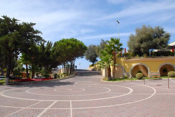 Piazza lastricata con alberi e un edificio giallo con archi.