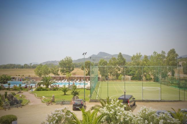 Campo da calcio recintato vicino a una piscina all'aperto. Sullo sfondo, colline e vegetazione.