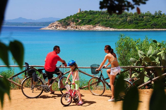 Famiglia in bicicletta davanti al mare turchese.