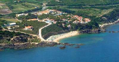 Vista aerea di un litorale con vegetazione, strutture turistiche, una piccola spiaggia e mare blu.