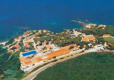Panoramica di un villaggio costiero con case rosse, piscina e vegetazione.