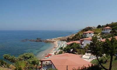 Case vicino a una spiaggia rocciosa con ombrelloni e mare calmo.