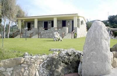 Edificio in pietra con scale e prato verde, incorniciato da rocce.