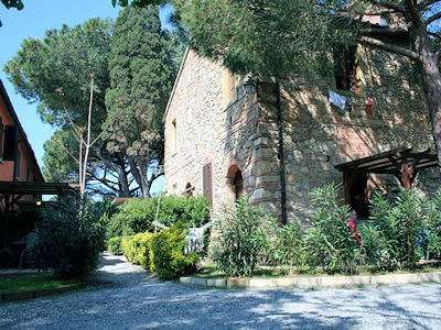 Edificio in pietra con alberi e arbusti circostanti, strada di ghiaia.