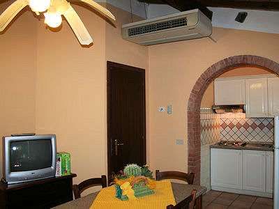 Sala da pranzo con tavolo, TV, ventilatore a soffitto e cucina con arco.