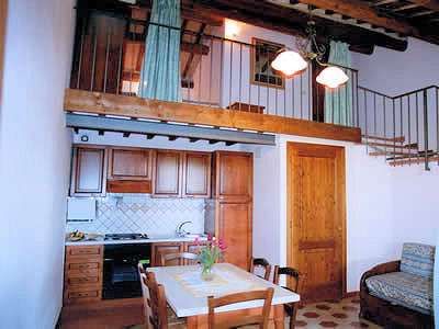 Cucina in legno con soppalco sopra, tavolo e sedie, e dettagli di travi a vista.