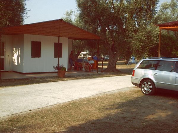 Una casa mobile con veranda in un campeggio. Vicino c'è un'auto parcheggiata.