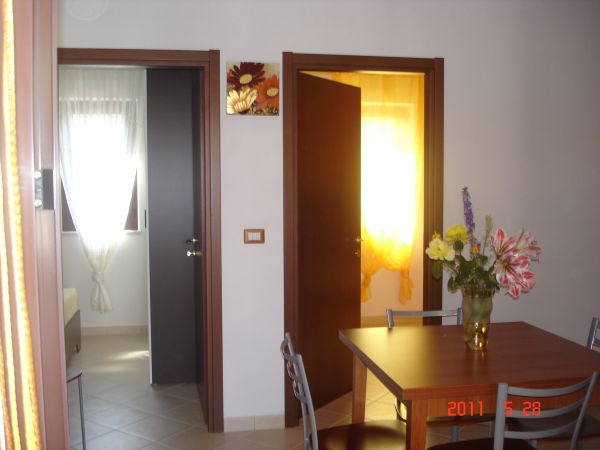Interno con tavolo, fiori e due porte aperte su stanze luminose.