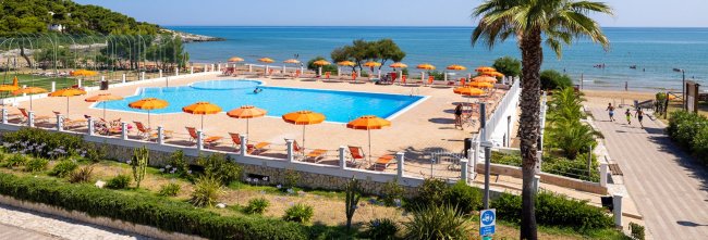 Piscina con lettini e ombrelloni arancioni vicino al mare.
