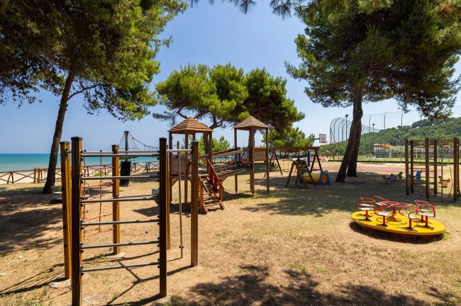 Parco giochi all'aperto vicino al mare, circondato da alberi.