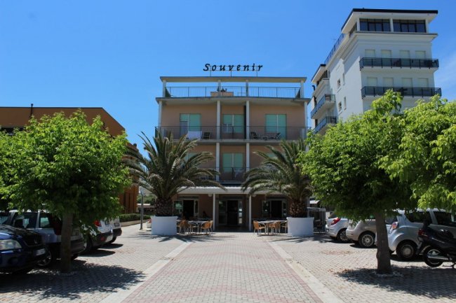 Facciata di un hotel con palme e tavolini all'aperto.