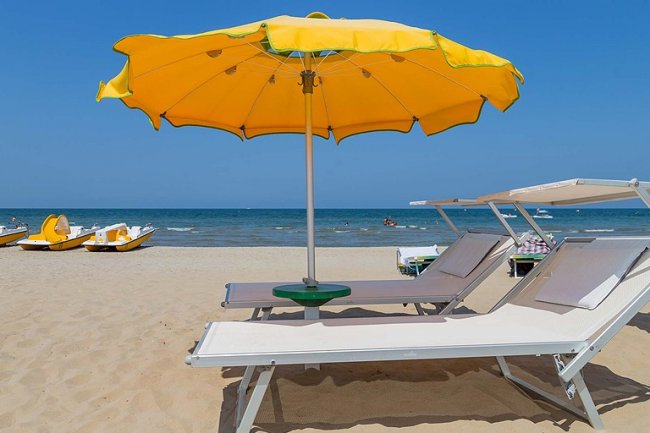 Spiaggia con lettini bianchi e ombrellone giallo.