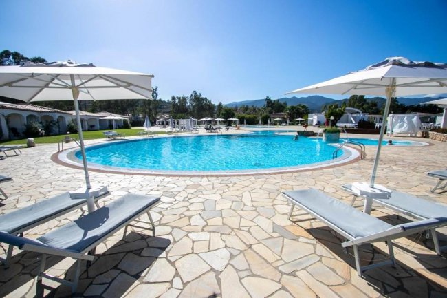 Piscina all'aperto con lettini e ombrelloni.