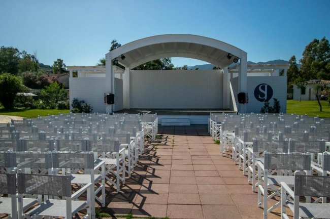 Palco all'aperto con sedie bianche disposte in file.