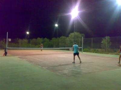 Campo da tennis illuminato di notte con tre persone che giocano.