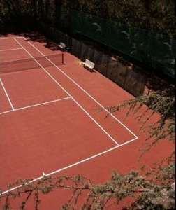 Campo da tennis in terra rossa con panchina e rete.