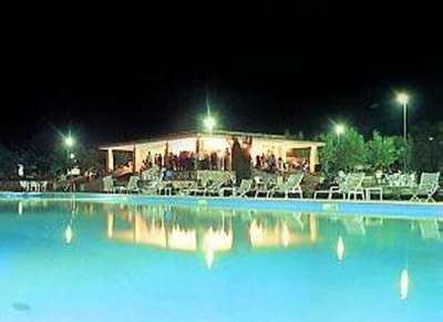 Piscina illuminata di notte con persone sotto un padiglione.