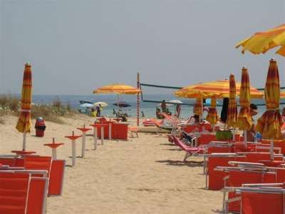 Spiaggia con sedie e ombrelloni giallo-arancio, persone in lontananza.