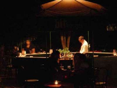 Persona dietro un bancone in un bar all'aperto, atmosfera serale con luci soffuse.