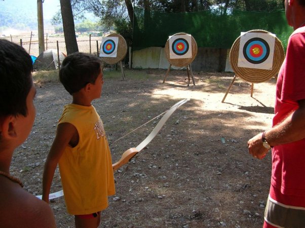 Bambino mira a bersagli con arco in un campo.
