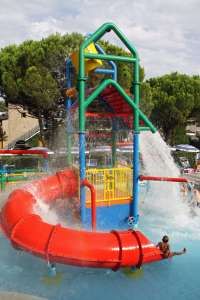 Gioco d'acqua colorato con scivolo rosso e getti d'acqua. Bambini giocano nella piscina sottostante.