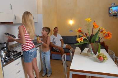 Famiglia in cucina. Donna cucina, bambino ride, uomo seduto.