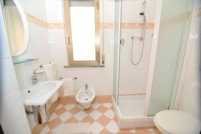 Bagno con cabina doccia, lavandino, bidet e finestra.