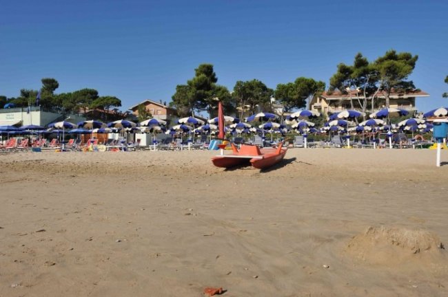 Spiaggia con pedalò e ombrelloni blu e bianchi.
