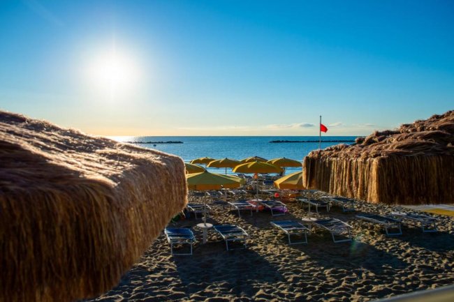 Spiaggia con ombrelloni gialli e sole basso sull'orizzonte.