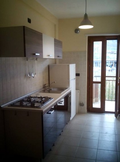 Cucina con piano cottura e frigo, porta-finestra sul fondo.