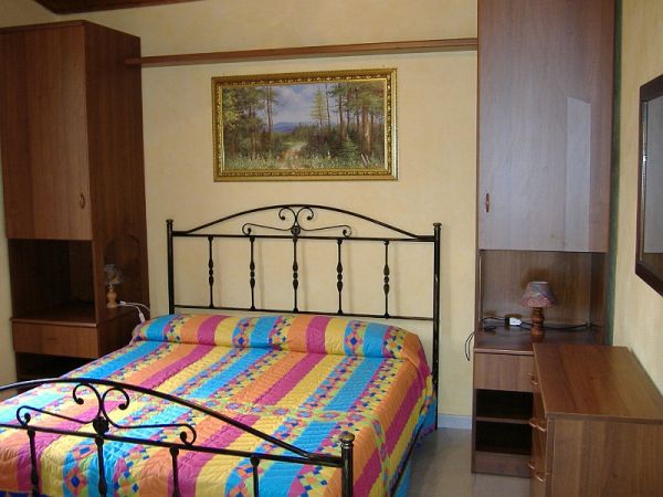 Camera con letto matrimoniale, coperta colorata, armadi di legno e quadro di paesaggio appeso.