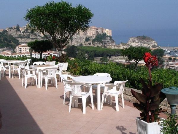 Terrazza con tavoli bianchi e vista panoramica su una città costiera.