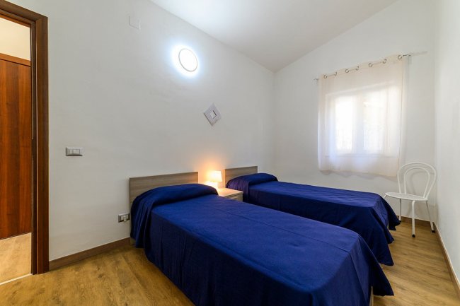 Camera con due letti singoli blu e luce soffusa.