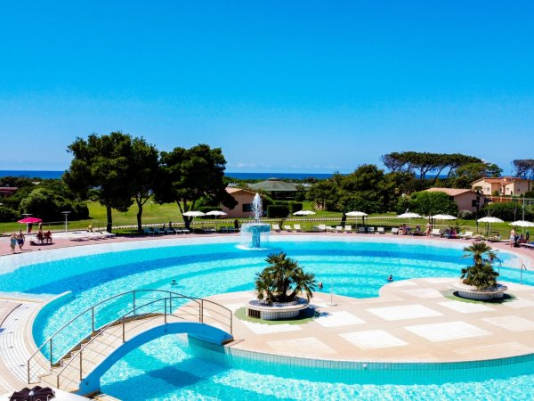 Una grande piscina all'aperto con una fontana centrale, circondata da alberi e sedie a sdraio.